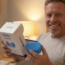 Hombre maduro sonriente sosteniendo la caja de Ronix NightFit y su estuche azul en un dormitorio.